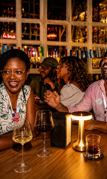 Diverse group of friends laughing at a cocktail bar with wine glasses and international flags.