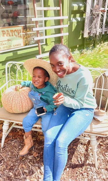 stay at home mom sitting on a bench with son, alongside a giant pumpkin