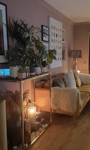 Cozy living room corner with a gold bar cart filled with green houseplants and a glowing candle.