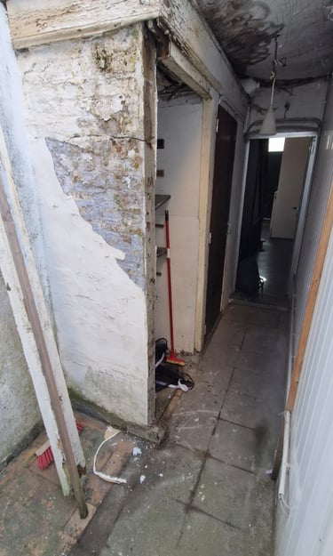 Couloir intérieur en cours de démolition avec murs dégradés, plafond effondré et traces d’humidité.