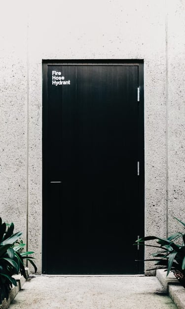 Foto a blanco y negro de una puerta negra cerrada al fondo de un pequeño pasillo.