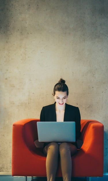 A woman sitting on a red chair with a laptop