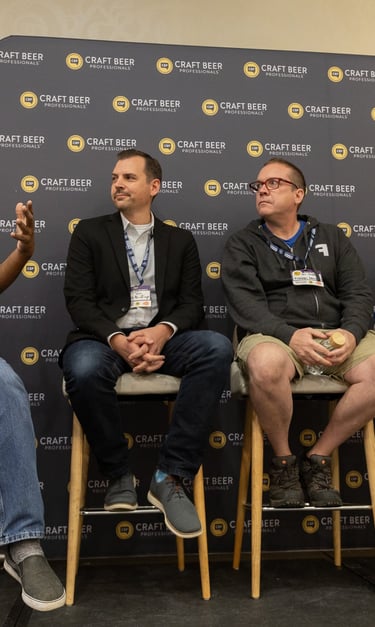 A panel of five craft beer professionals speaking at a conference event with a branded backdrop.