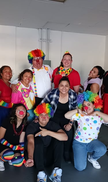 A diverse group of people posing in colorful clown costumes with rainbow wigs and red noses.