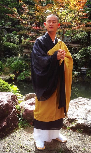 Buddhist monk in traditional yellow and black robes standing in a serene Japanese zen garden.