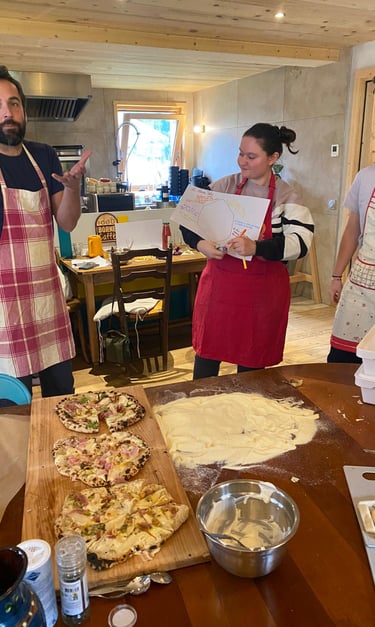 Three people in aprons participate in a hands-on homemade pizza making workshop in a rustic kitchen.