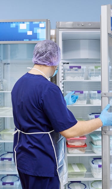 Laboratory technician in blue scrubs organizing samples in a medical laboratory refrigerator.