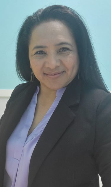 Professional portrait of a smiling woman in a black blazer and lavender shirt against a blue background.