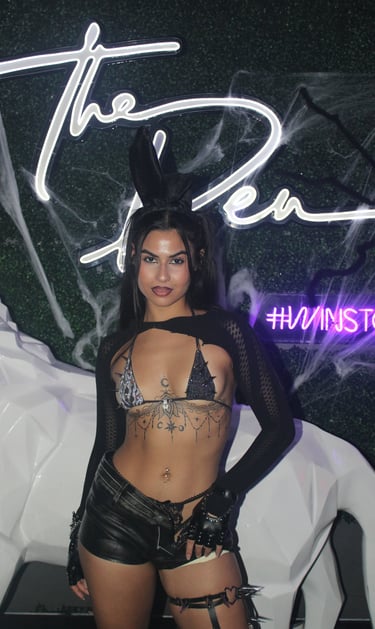 Woman in a black bunny costume and sequin bikini top poses at a Halloween party.