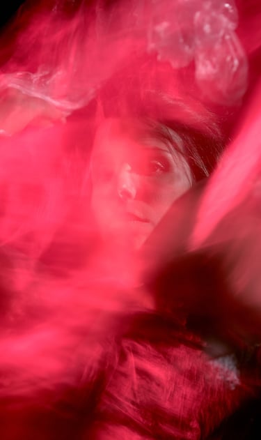 Dramatic artistic portrait of a woman peering through translucent layers of vibrant red fabric.