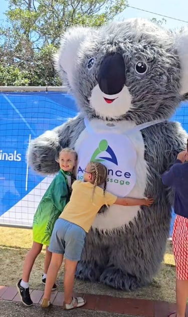 two children hugging a huge Advance Body Massage Koala Mascot
