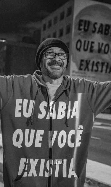 Homem com braços abertos e texto projetado no peito "eu sabia que você existia"