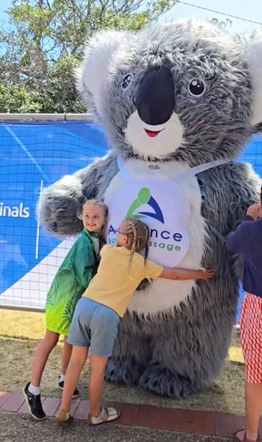 two children hugging a huge Advance Body Massage Koala Mascot