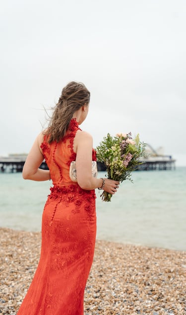 Bride in red dress standing on the beach looking at the sea