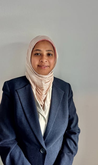 Professional portrait of a smiling woman wearing a pink hijab and dark blue blazer.