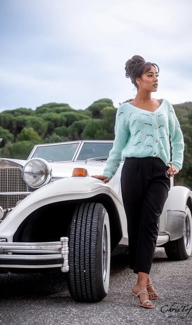 Femme en gilet mint posant devant une voiture de collection blanche en extérieur à Valmy 66.