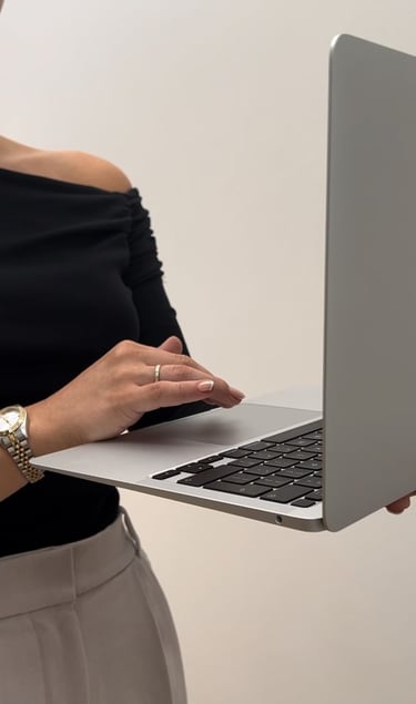 Woman in a black off-shoulder top working on a laptop, holding it with one hand while typing.