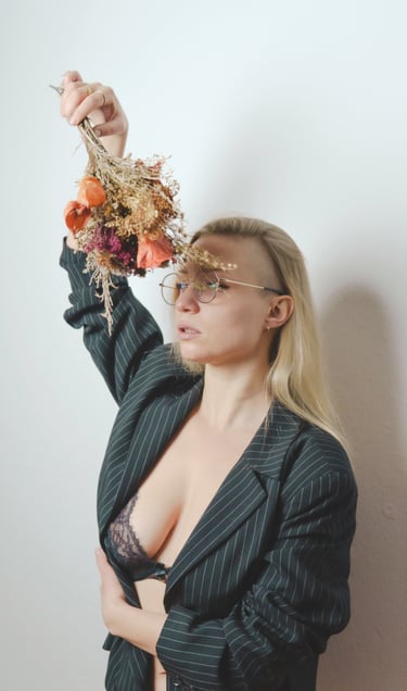 a woman in a suit and glasses holding a bouquet posing for a photo