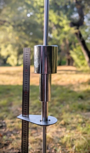 A dynamic cone penetrometer tool for soil testing standing beside a measuring ruler in a field.