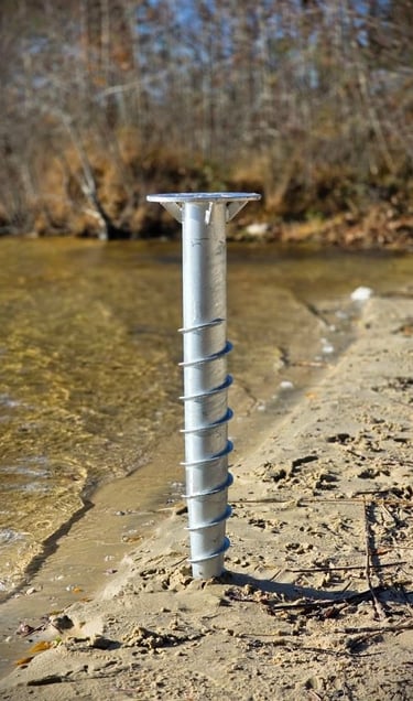 A galvanized steel screw pile foundation installed in the sandy shore of a lake for dock construction.