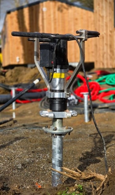 Portable hydraulic ground screw driver installing a steel pile foundation at a construction site.