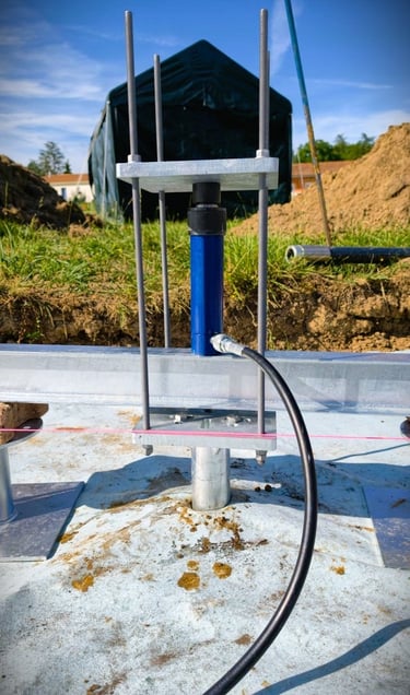 A blue hydraulic jack testing the load capacity of a metal ground screw foundation at a construction site.