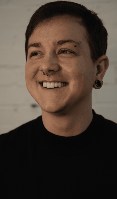 Sam, a non-binary trans-masculine white person with dark, short hair smiles and looks to their right