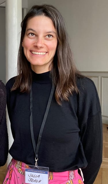 Julia Braun lächelt freundlich; braunes schulterlanges Haar, schwarzer Rollkragenpullover 