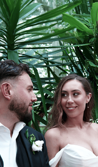 Bride and groom seated together in front of a lush tropical plant, smiling and enjoying their special moment.