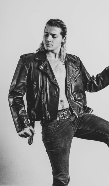 a man in a leather jacket and jeans posing for a photo