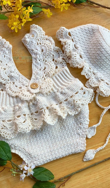 Handmade cream crochet baby romper with ruffled collar and matching sun hat on a wooden background.