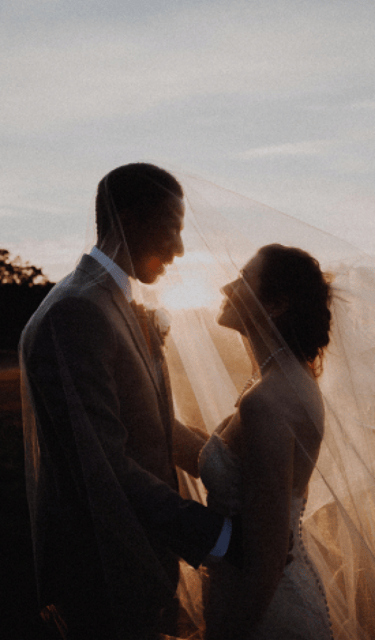a bride and groom standing in front of a sunset