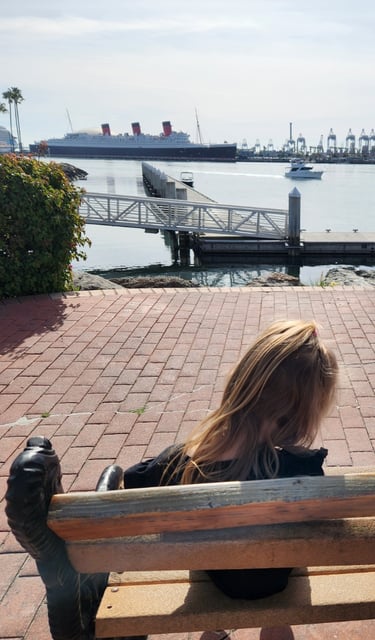 Child sitting on a waterfront bench at Shoreline Village in Long Beach with views of the Queen Mary