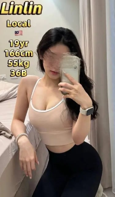 A fit woman in a pink sports bra and black leggings takes a mirror selfie in a bedroom.