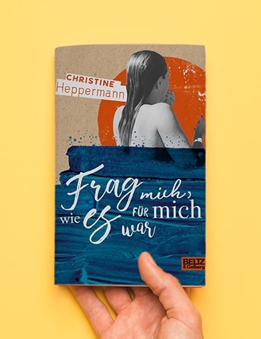 Eine Hand auf gelben Untergrund hält das Buch "Frag mich, wie es für mich war."