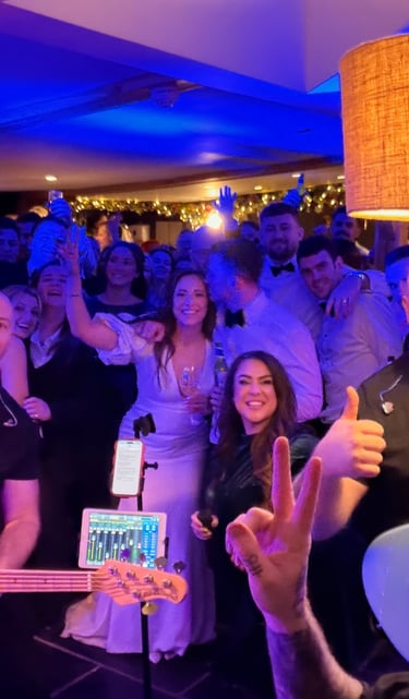A professional live wedding band performs for a cheering crowd at a lively indoor reception.