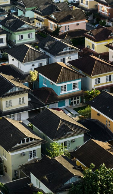 Aerial view of a dense suburban residential neighborhood with colorful modern houses and tropical trees.