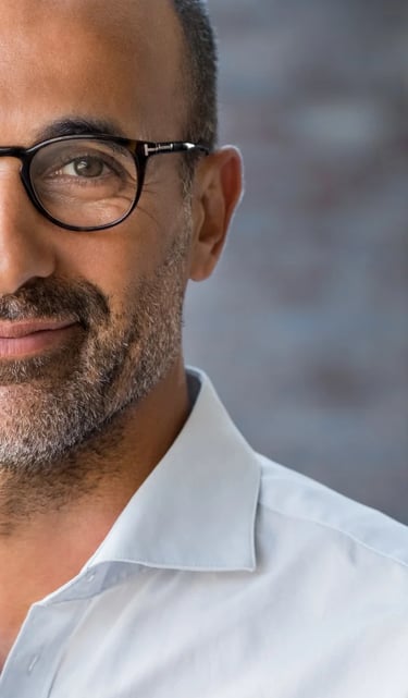 Portrait of a smiling professional man wearing black frame glasses and a white button-down shirt.