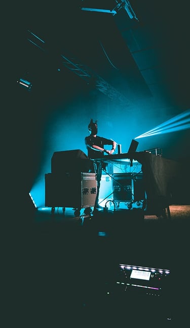 Vagues de lumières colorées projetées sur un DJ en pleine immersion dans son mix, capturées par Thomas Bordas.