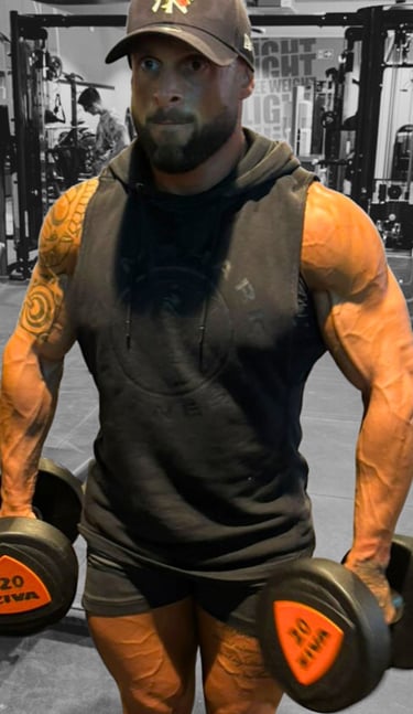 Romain Pittier, coach sportif musclé en salle de sport, tenant des haltères de 20 kg, prêt à guider ses clients vers leurs ob