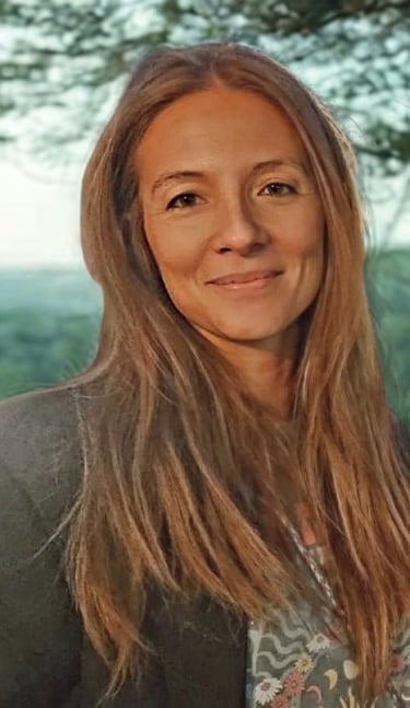 Smiling woman with long blonde hair outdoors in a natural green background.