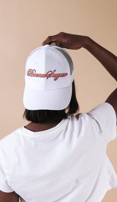 A person from behind wearing a white Bronx Sugar trucker hat and a matching t-shirt.
