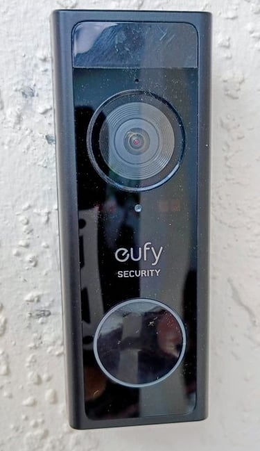 Black Eufy security camera and doorbell mounted on home white vexterior wall