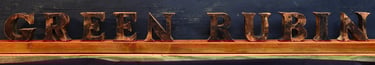 Kunstvoller Schriftzug der Marke Green Rubin in dunkel bemalten Lettern auf einem Holzbalken