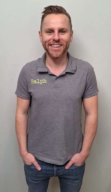 een man in een grijs shirt en broek die voor een muur staat