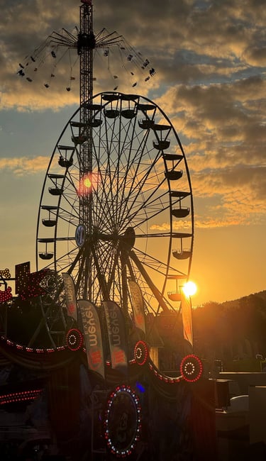 Silhouette of a Ferris wheel and carnival swing ride against a golden sunset sky at a fair.