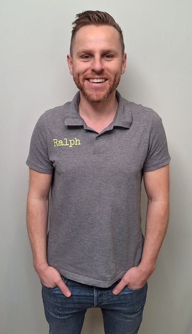 een man in een grijs shirt en broek die voor een muur staat