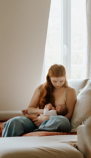 portrait de maman allaitant son nouveau né assise sur son canapé lumière douce en intérieur