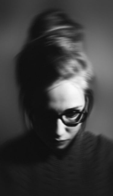 A young woman looking down at her phone with a dejected expression, her body language reflecting the