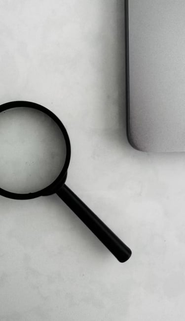 Foto a blanco y negro de una lupa y una laptop sobre un escritorio.